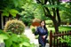 A woman in a blue kimono holding a fan in a garden.