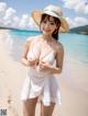 A woman in a white dress and straw hat on a beach.